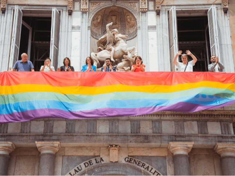 Desplegament de la bandera LGTBI+ a la balconada principal del Palau de la Generalitat. Fotografia distribuïda per la Generalitat de Catalunya. Autor Arnau Carbonell